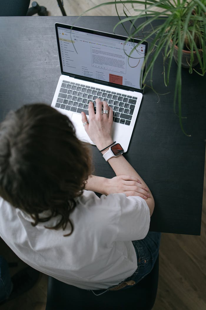 A person sits at a black table, using a laptop for work in an indoor office setting.
